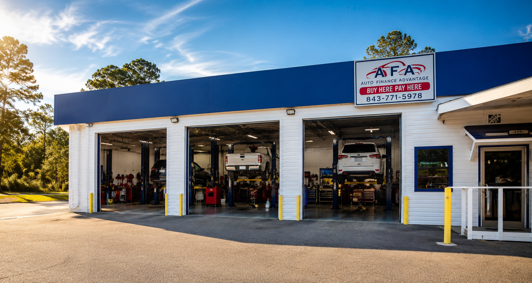 Auto repair shop with three bays open and vehicles on lifts under a blue awning in sunlight.